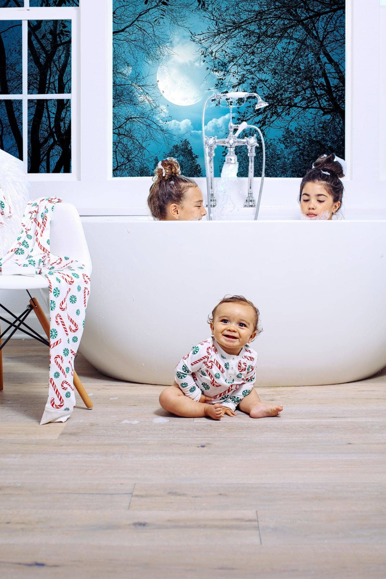 girls in bathtub with smiling toddler on floor