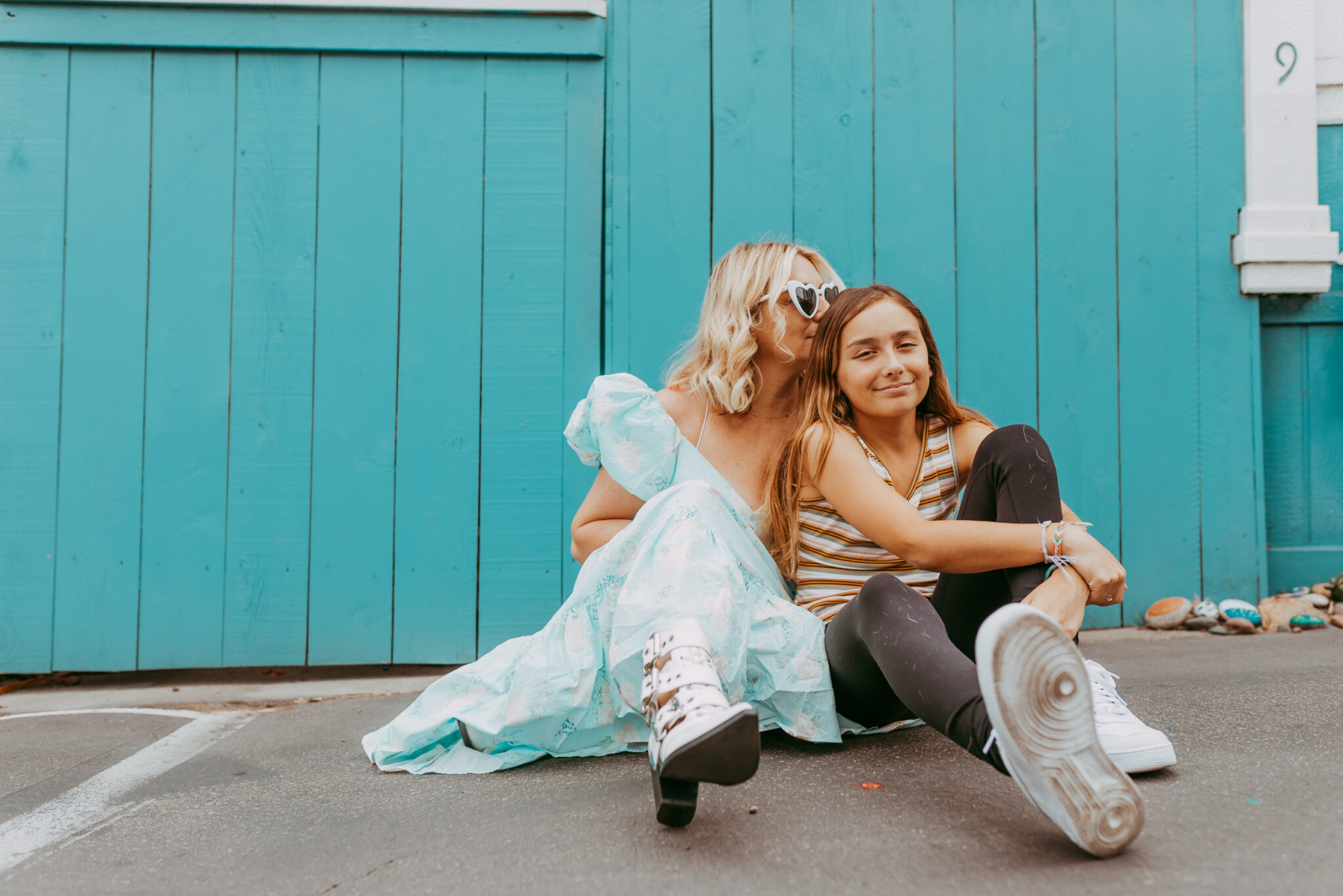 A mom and daughter sit on the concrete hugging.