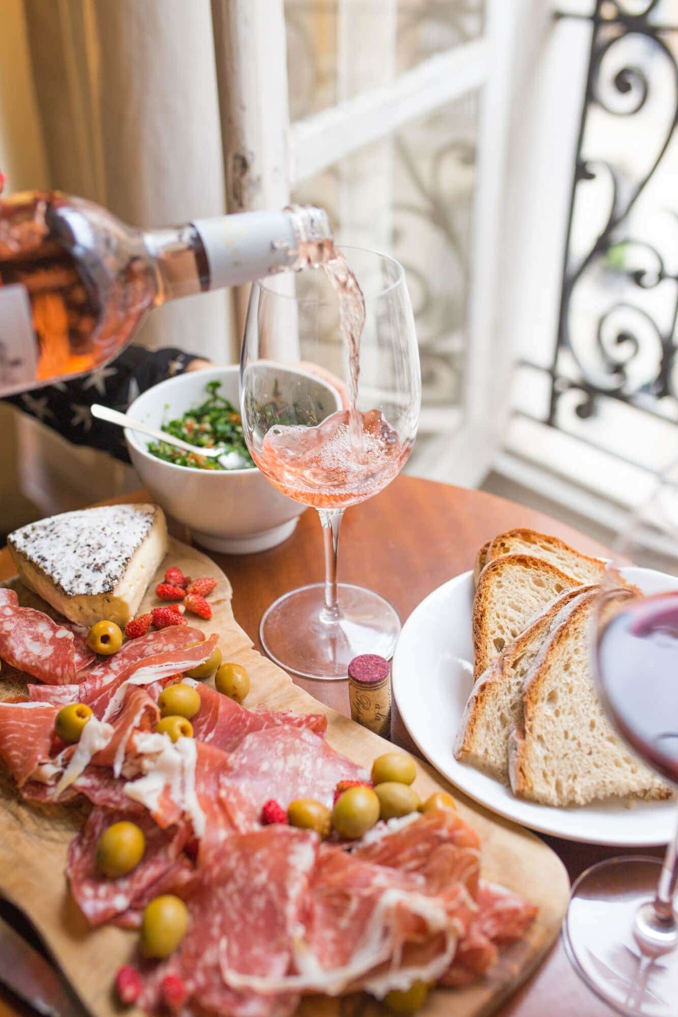 pouring wine into a glass beside a platter of food