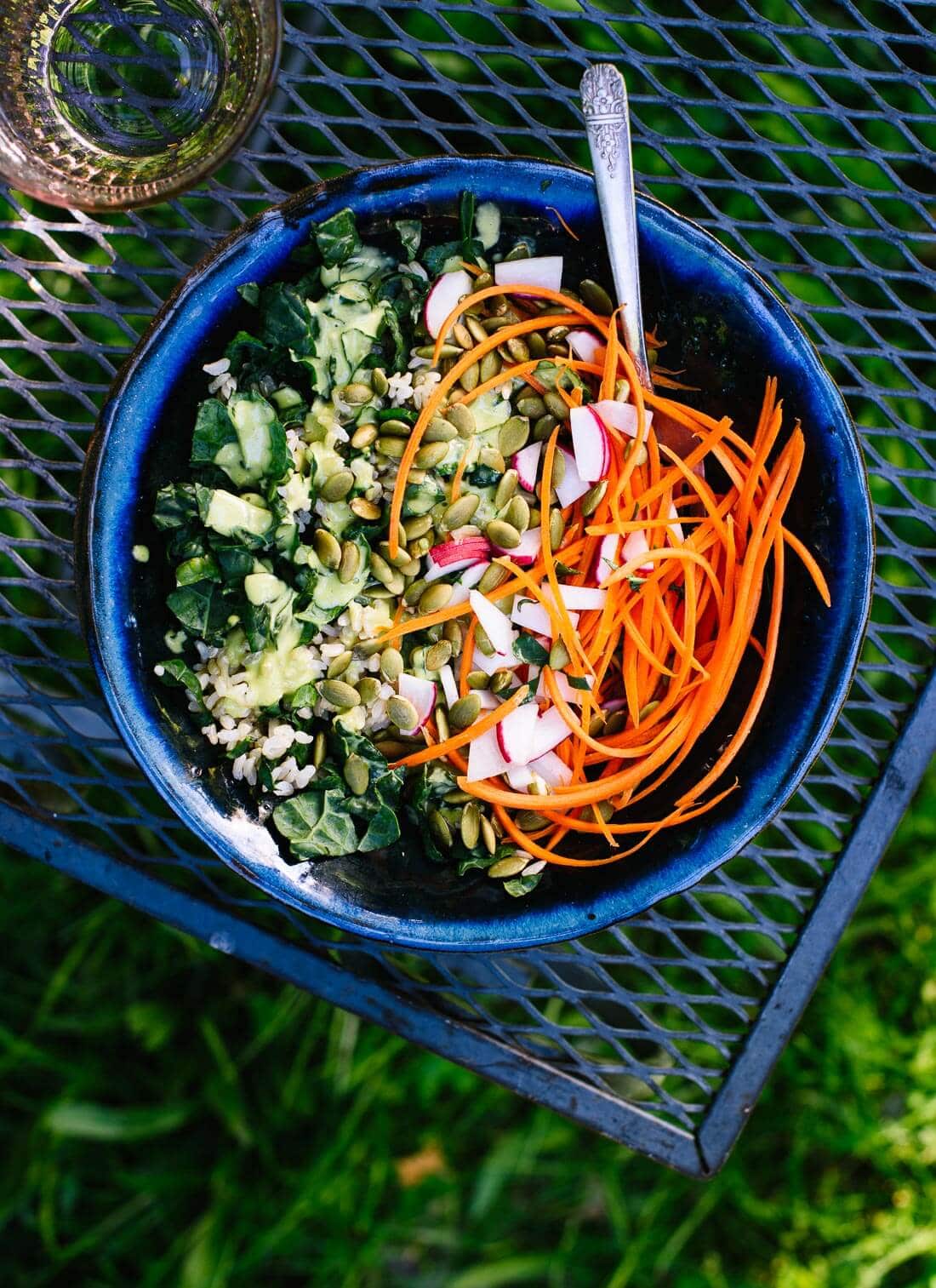 A beautiful kale salad topped with fresh vegetables, and green tahini dressing.