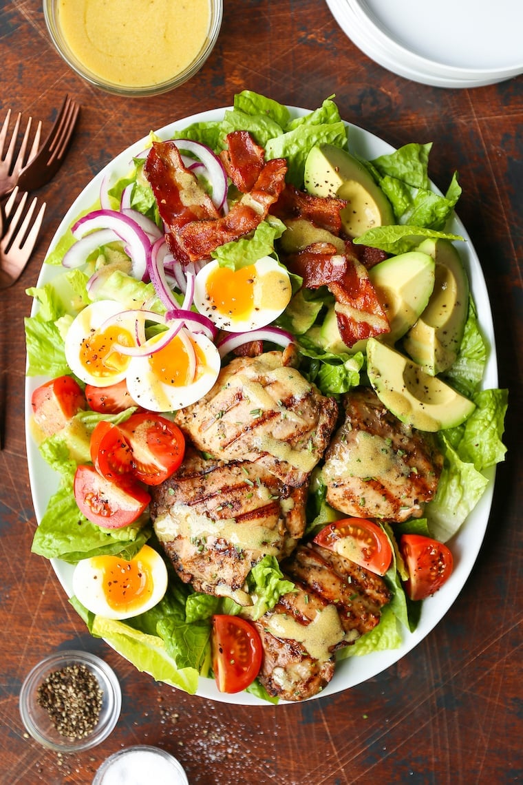 Overhead view of a large  white oval platter loaded up with a chicken cobb salad. 