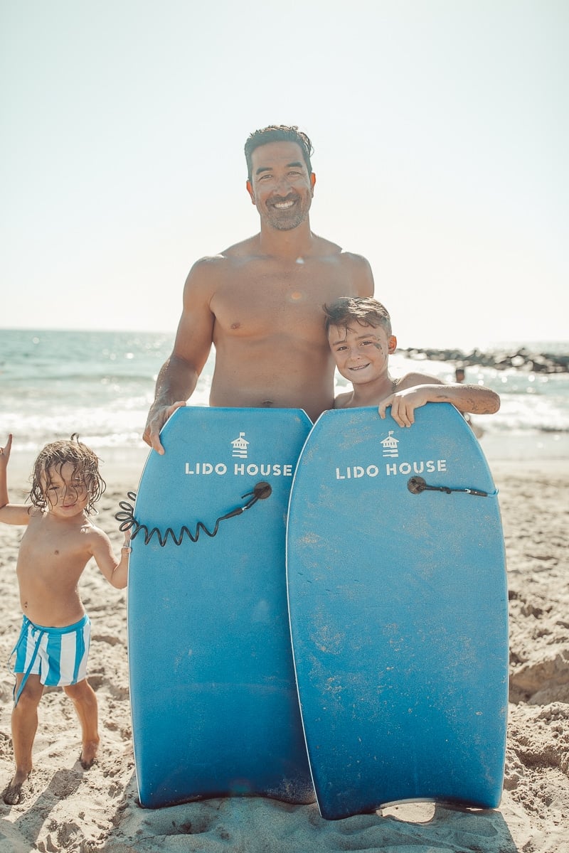 father and sons at beach with boogie boards