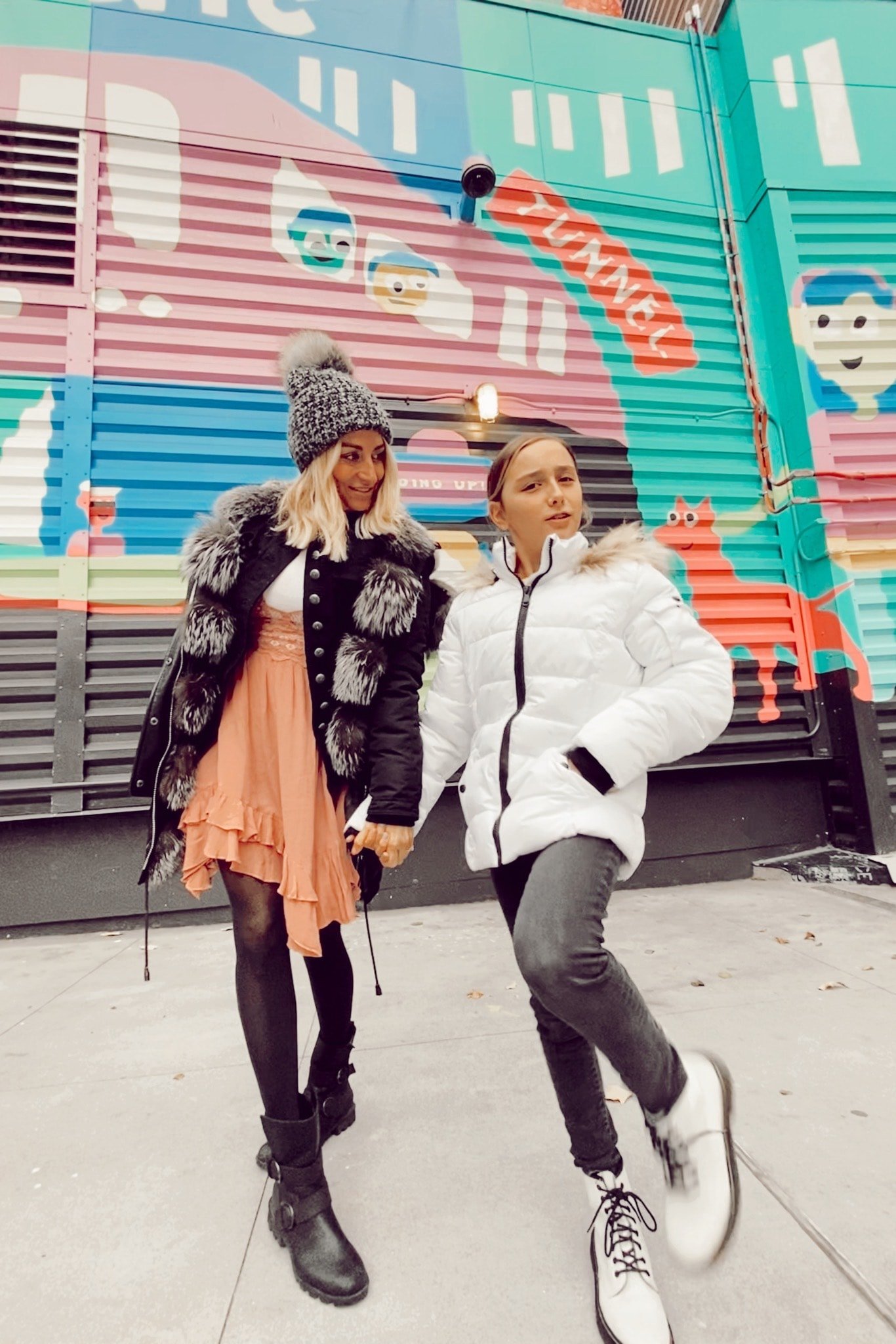 mother and daughter walking by mural