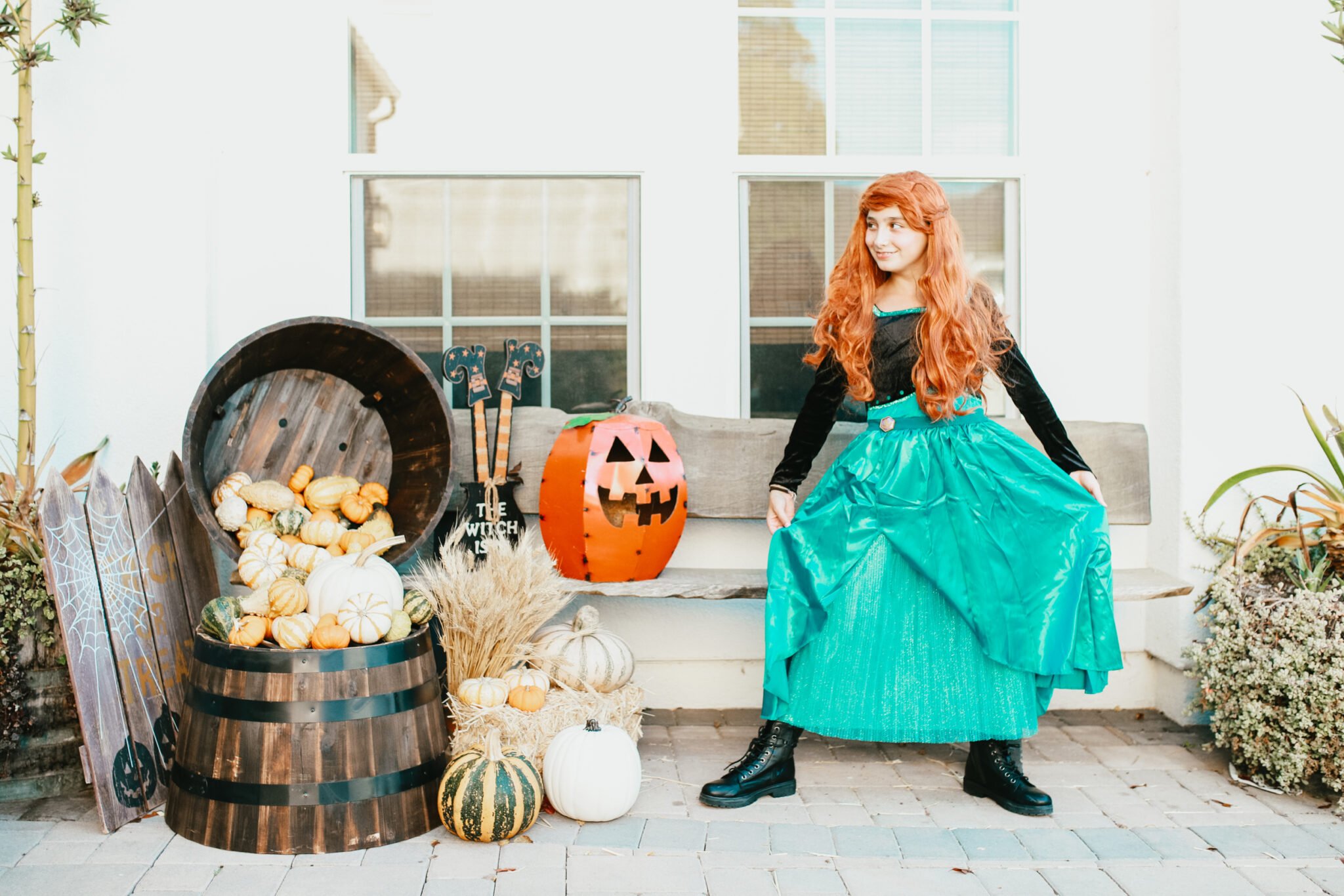 A girl is dressed like a Disney princess for Halloween and stands next to a jack-o-lantern. 