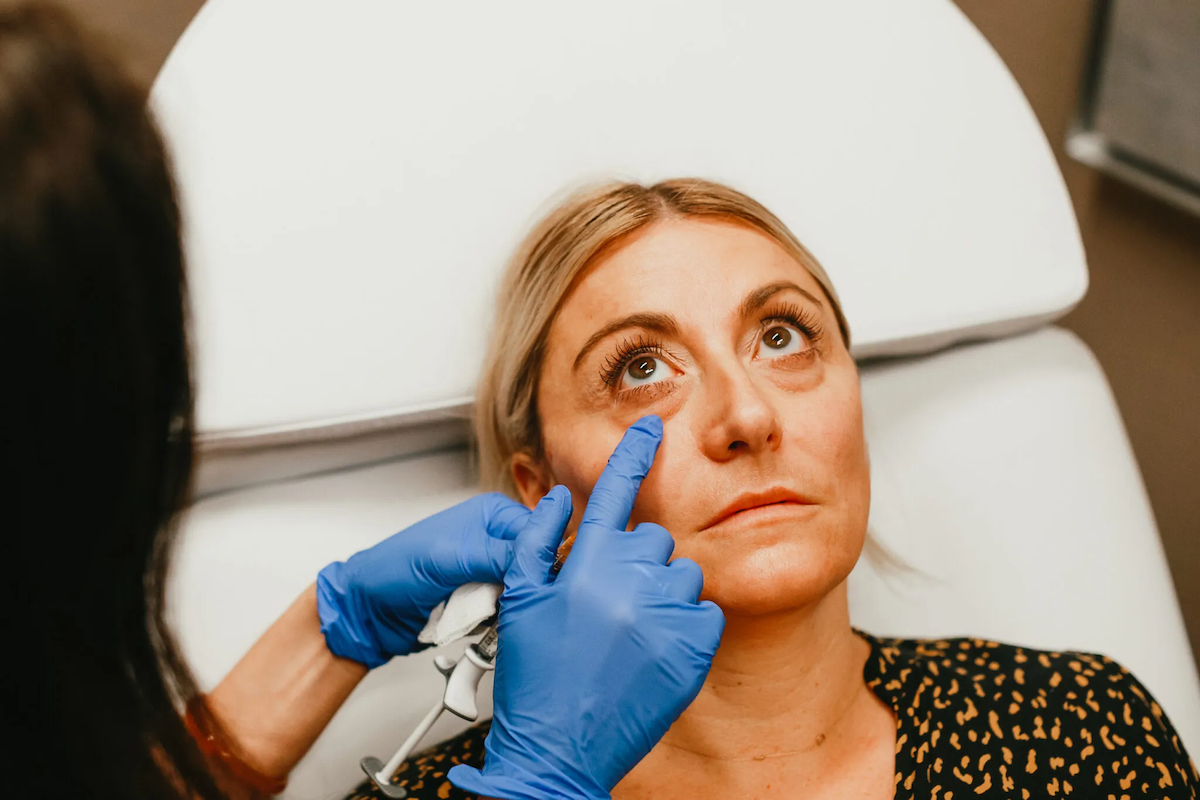 A medical assistant touches a woman's undereye as she lays in a white medical chair before having botox.