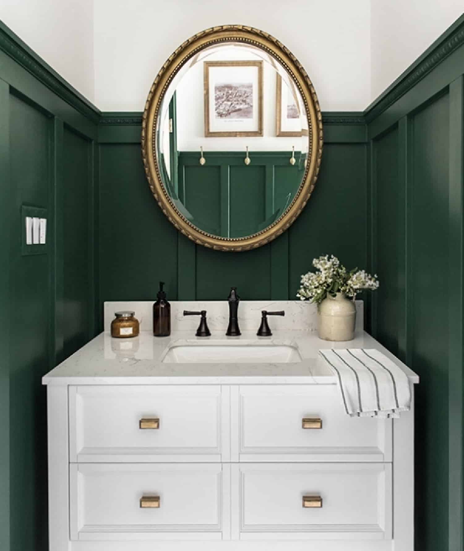Sophisticated modern farmhouse bathroom with green wainscoting walls, a polished white sink and gold mirror.