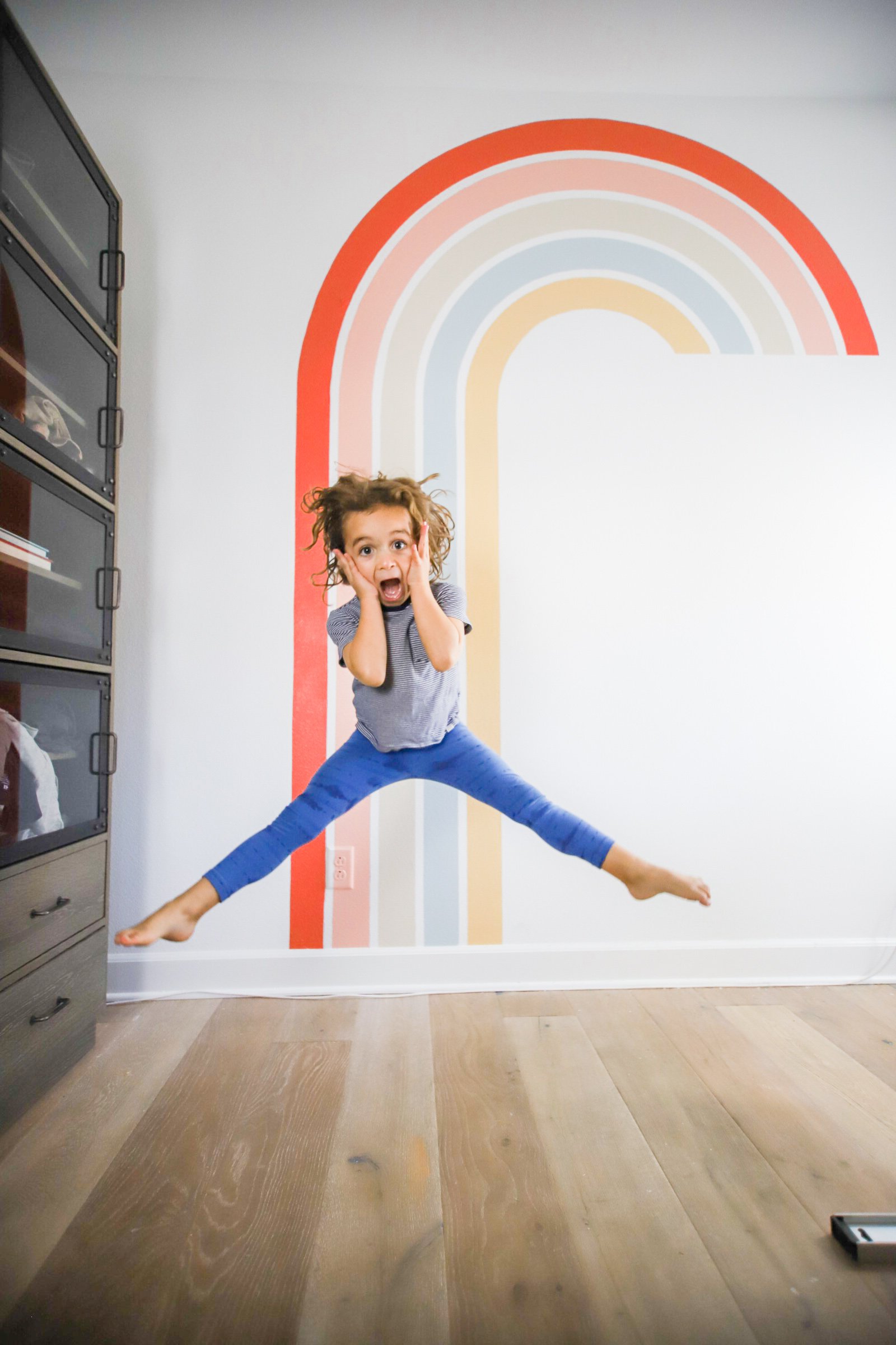 kid jumping in front of rainbow mural