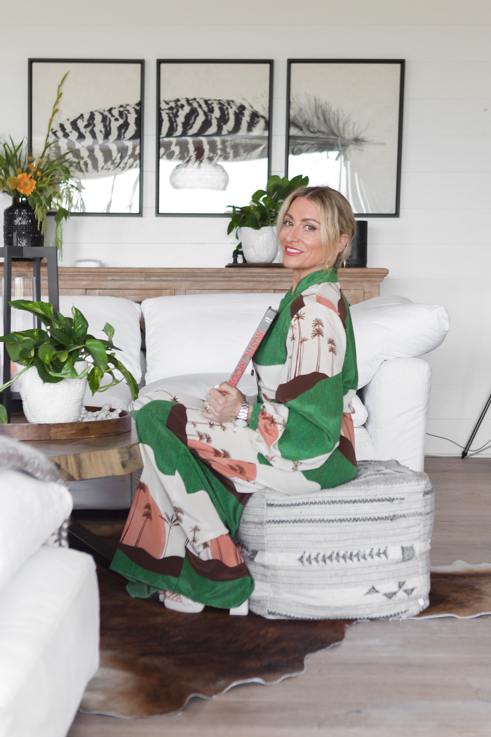 A woman sitting in her living room in a green and pink dress.