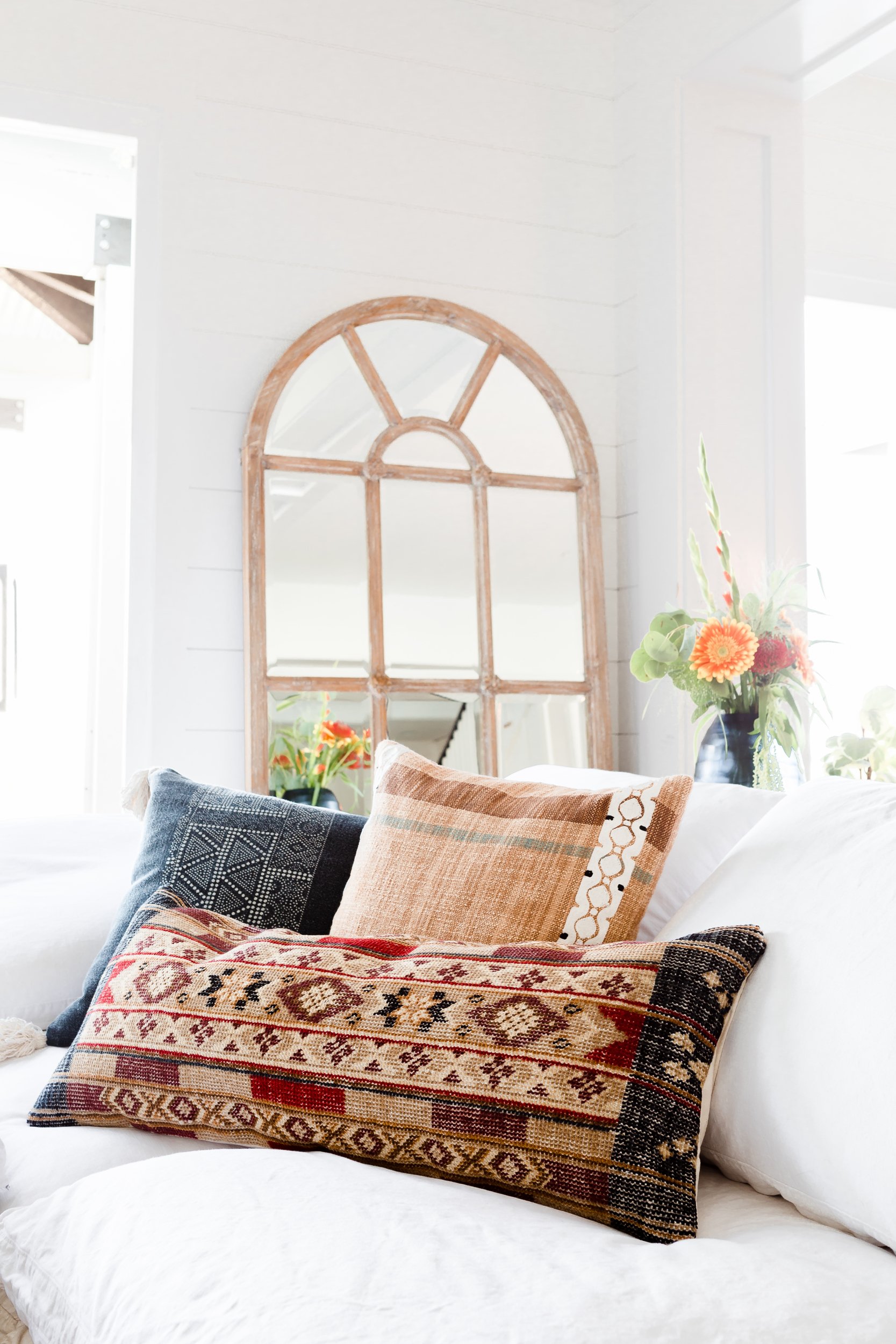 Throw pillows on a couch and a mirror leaning on the wall in the background of a living room.