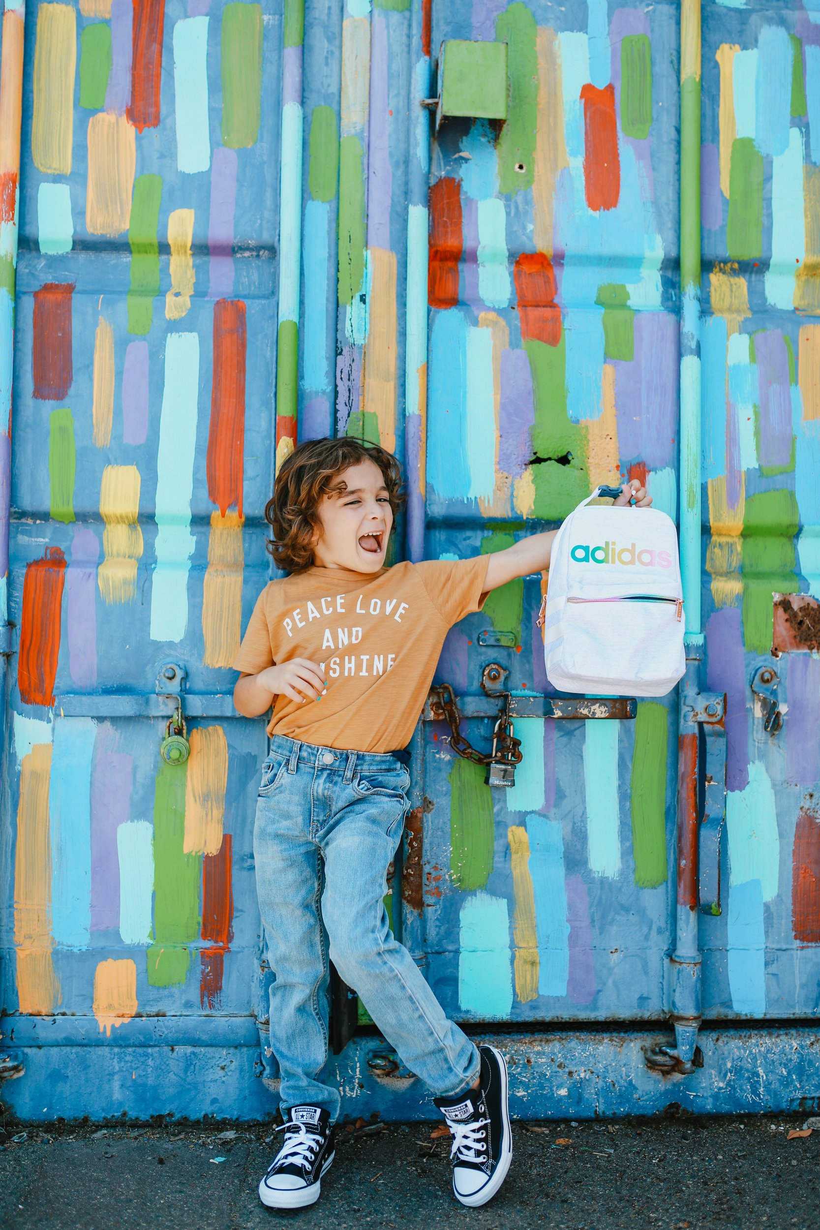 boy holding a backpack by mural