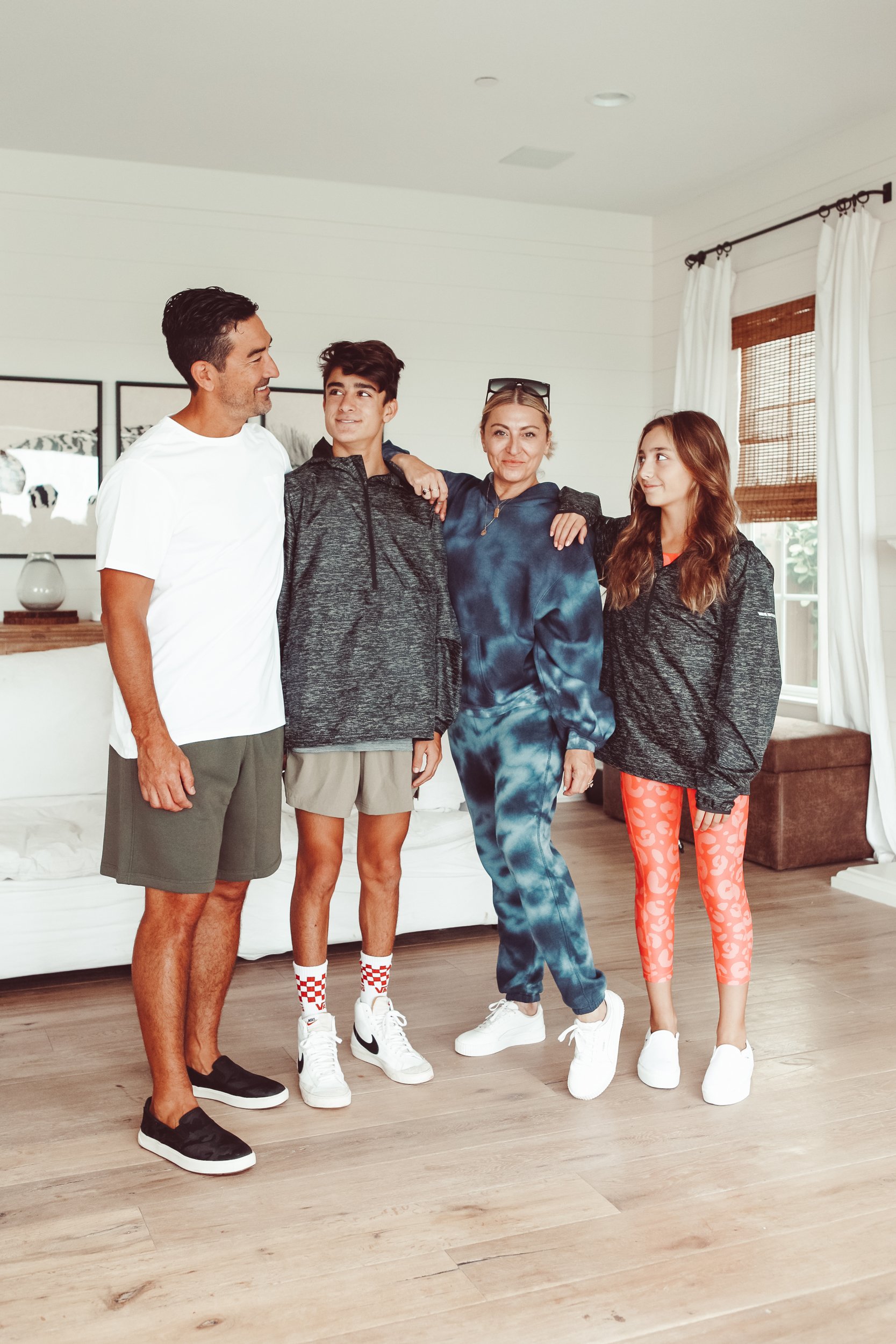 A mom and dad stand in the living room with their teenage son and daughter.