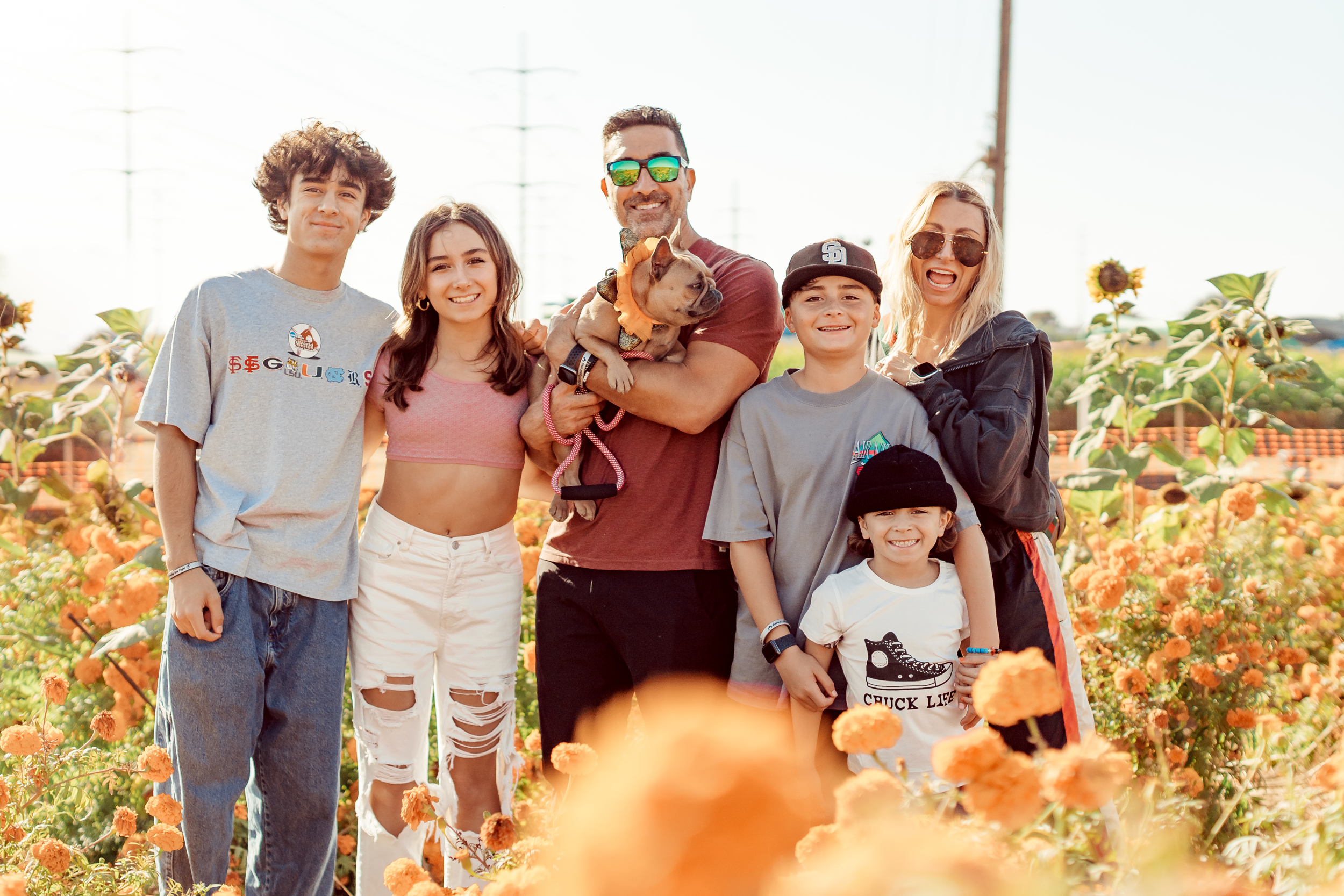 A family of six and their dog stand outside in an orange flower field.