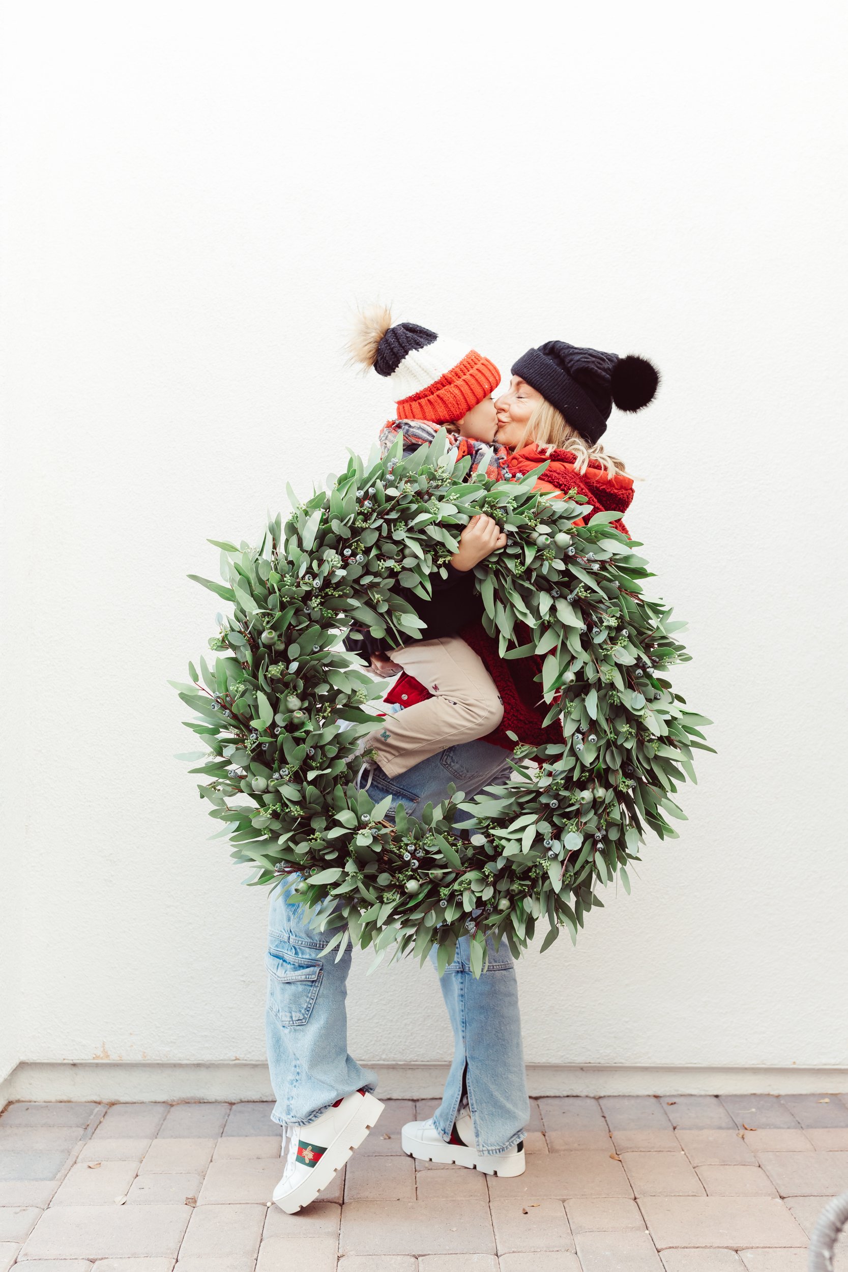 mom kissing her toddler while holding a wreath