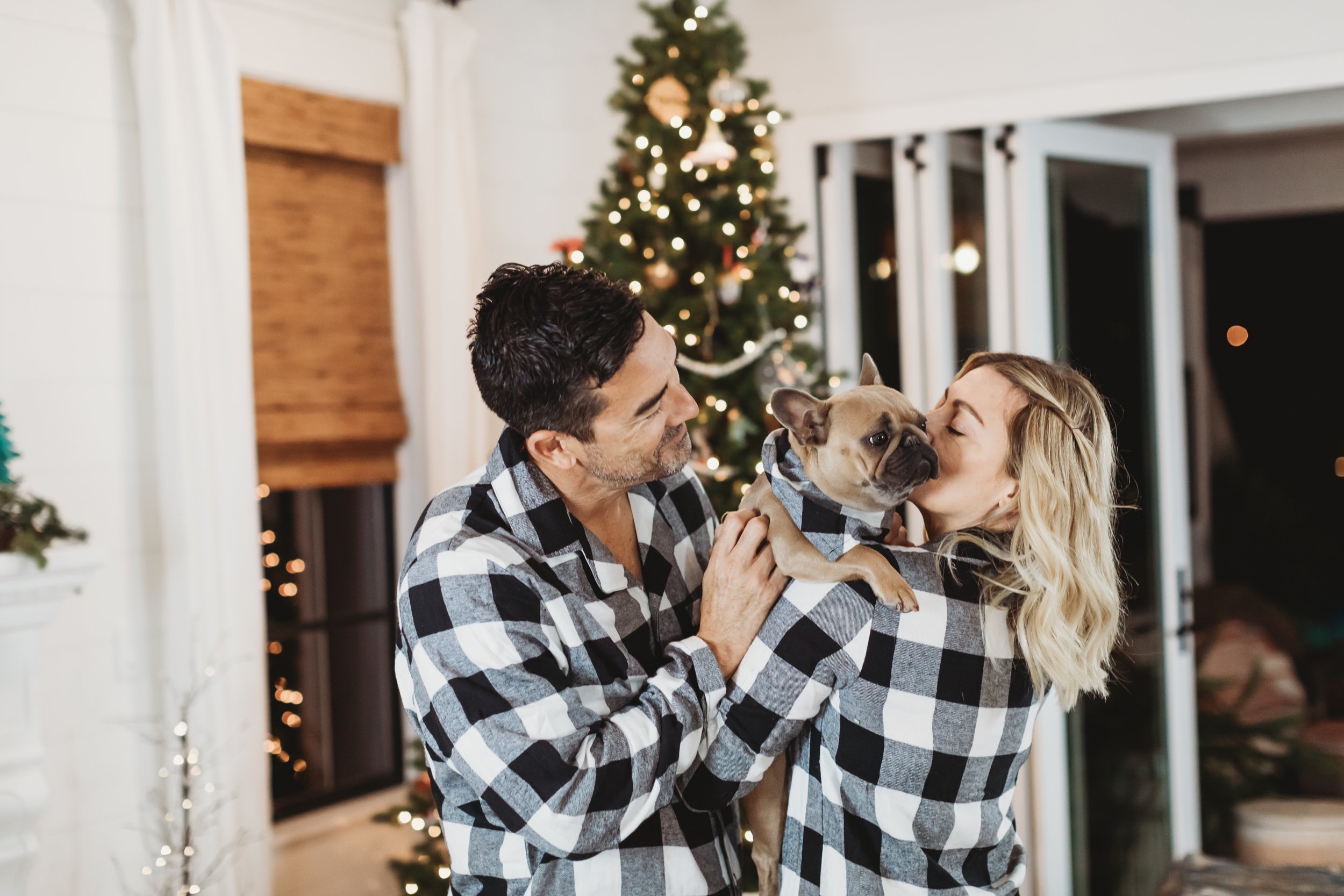 couple holding their dog by the christmas tree