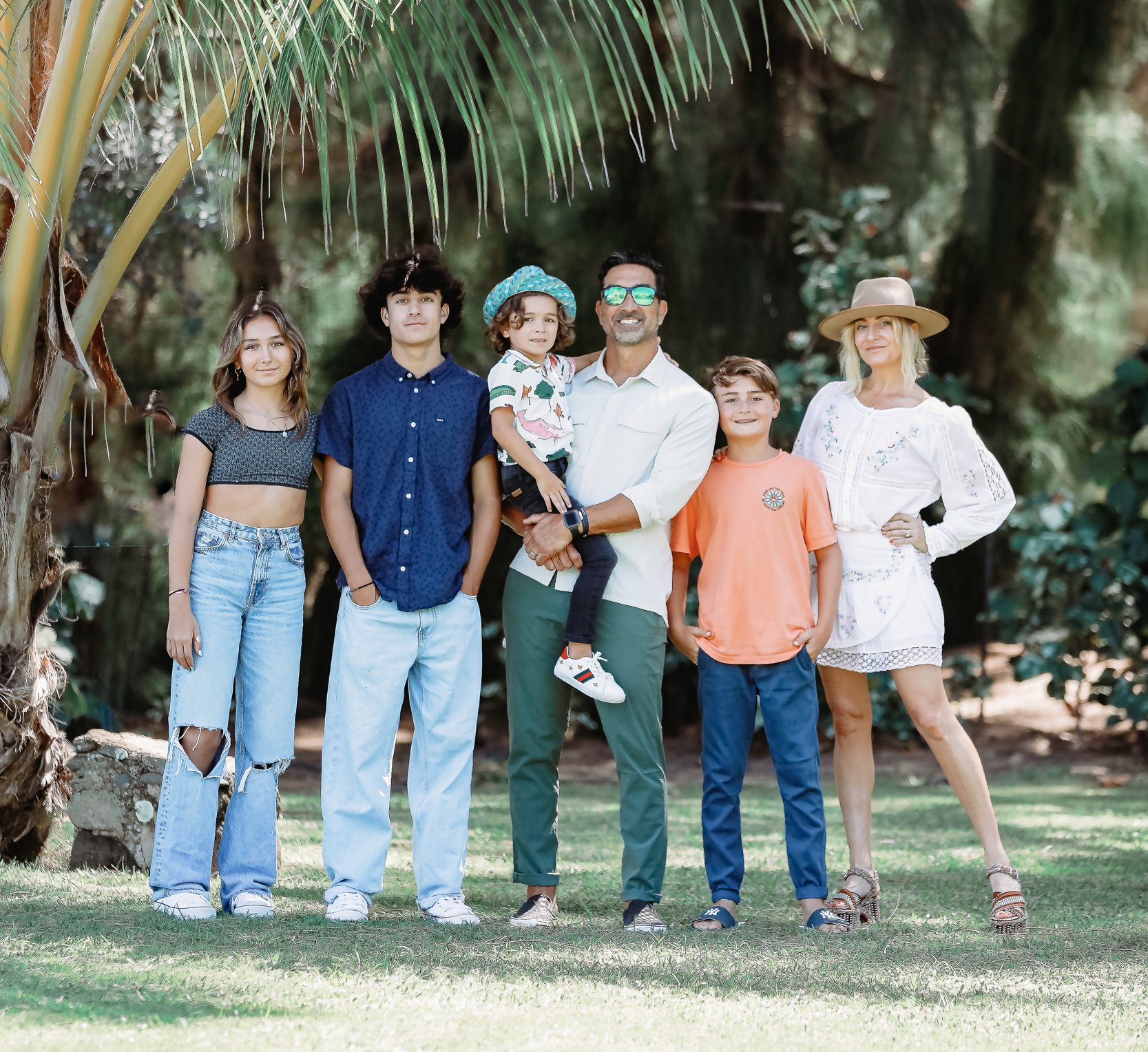 A family is standing together outside under the palm trees in Hawaii.