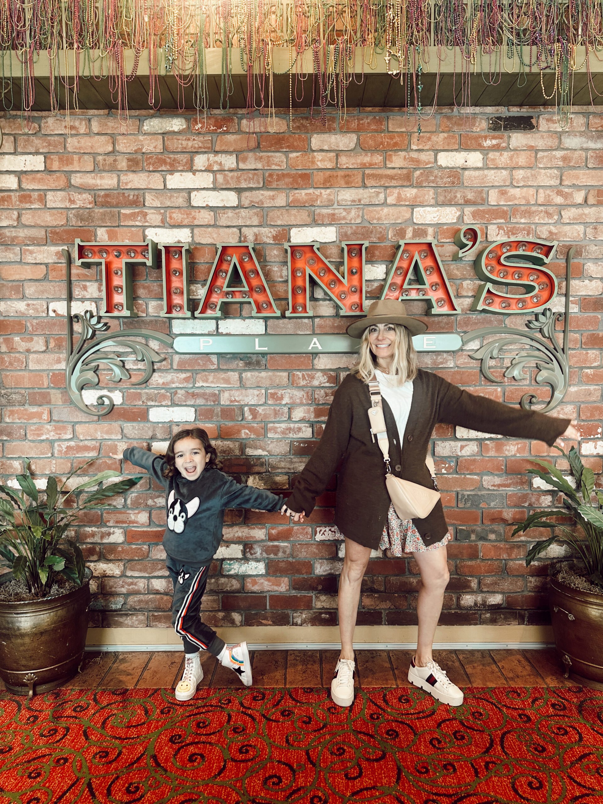 A boy and his mom are dancing in front of a restaurant sign. 