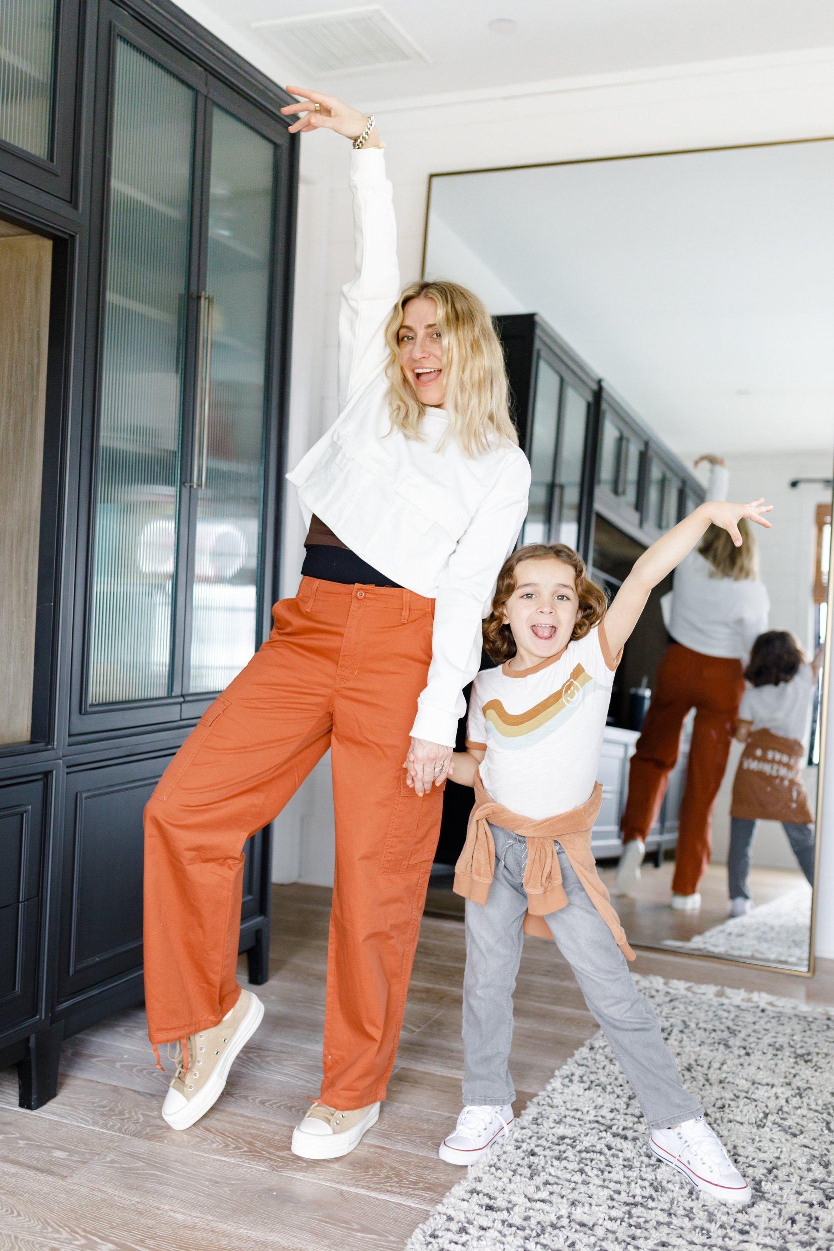 A mom and her son are dancing around a bedroom with their arms in the air.