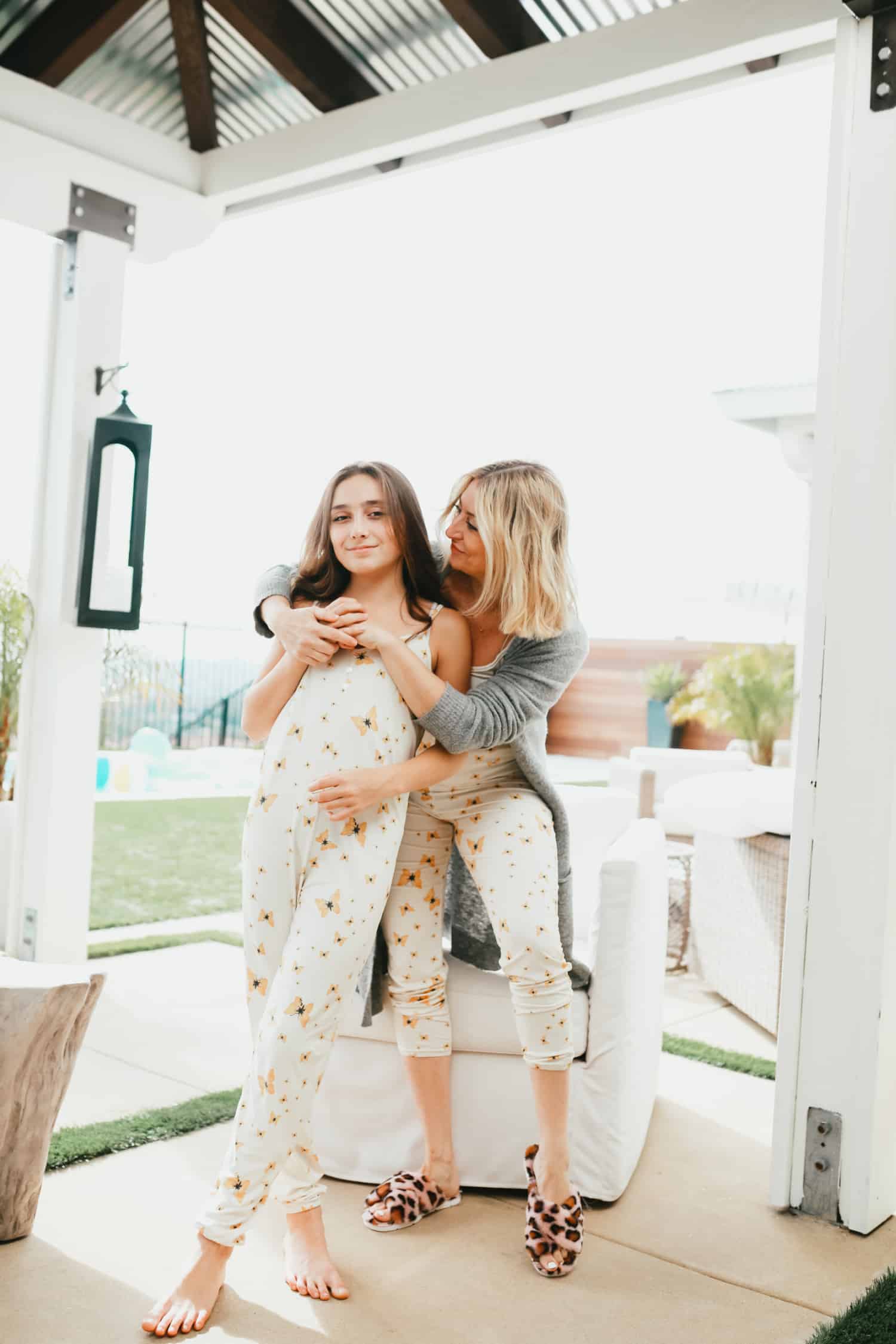 Attractive mother and daughter wearing matching pajamas. The mother is wearing a grey robe and has her arms wrapped around the girl. 