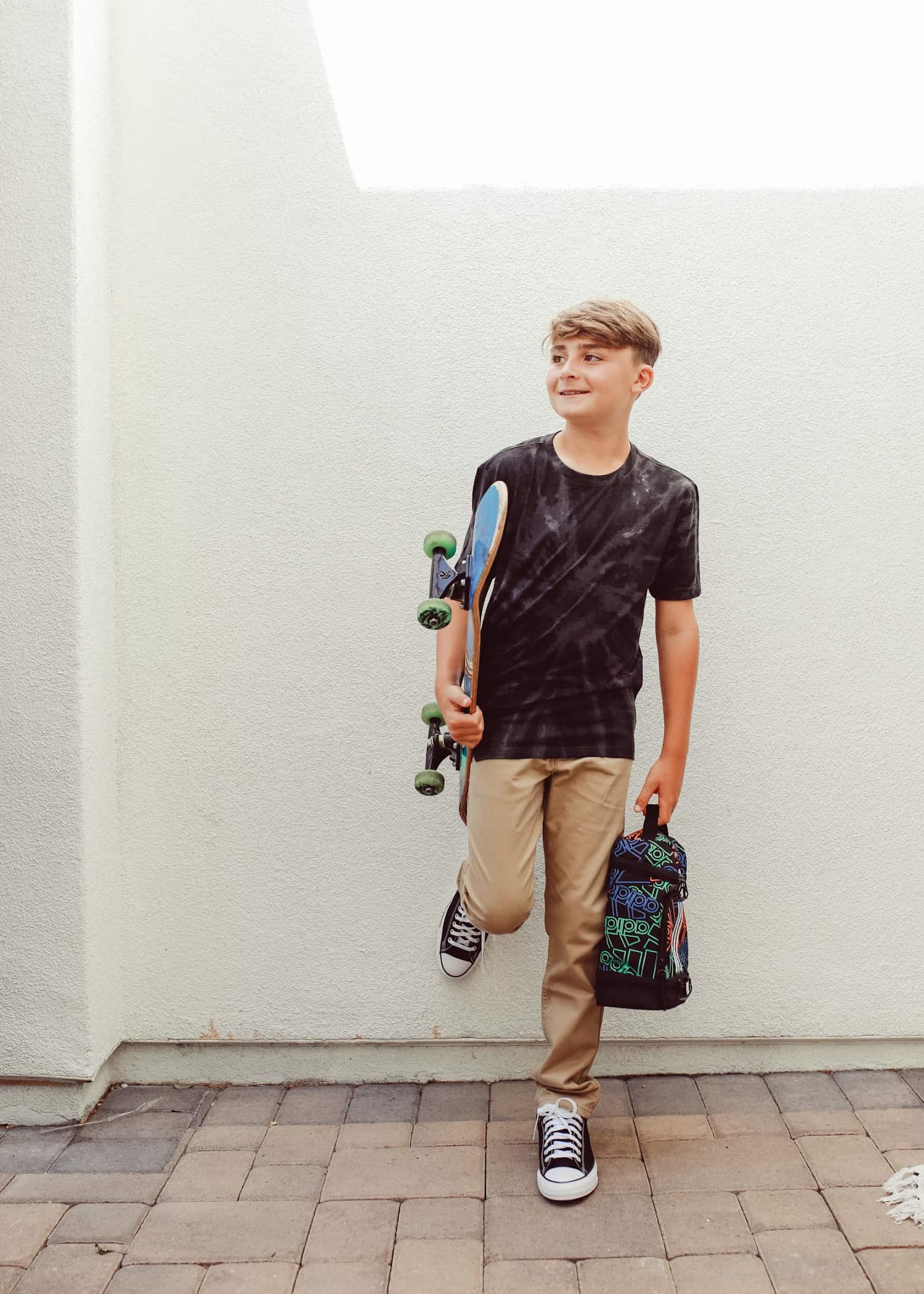 A good example of a casting profile picture. The young teenager is leaning against a wall with his head turned to one side. He's holding a backpack and a skateboard.