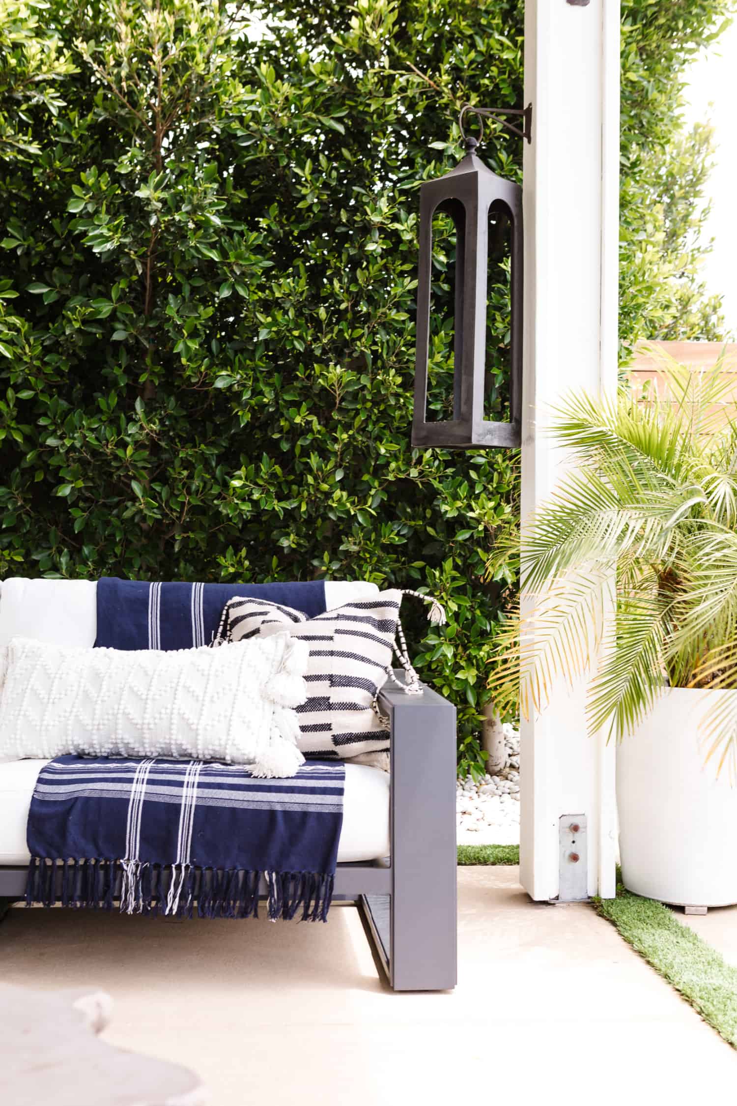 A cozy outdoor seating area with white and blue pillows and blankets. A large palm in a planter is off to the side.