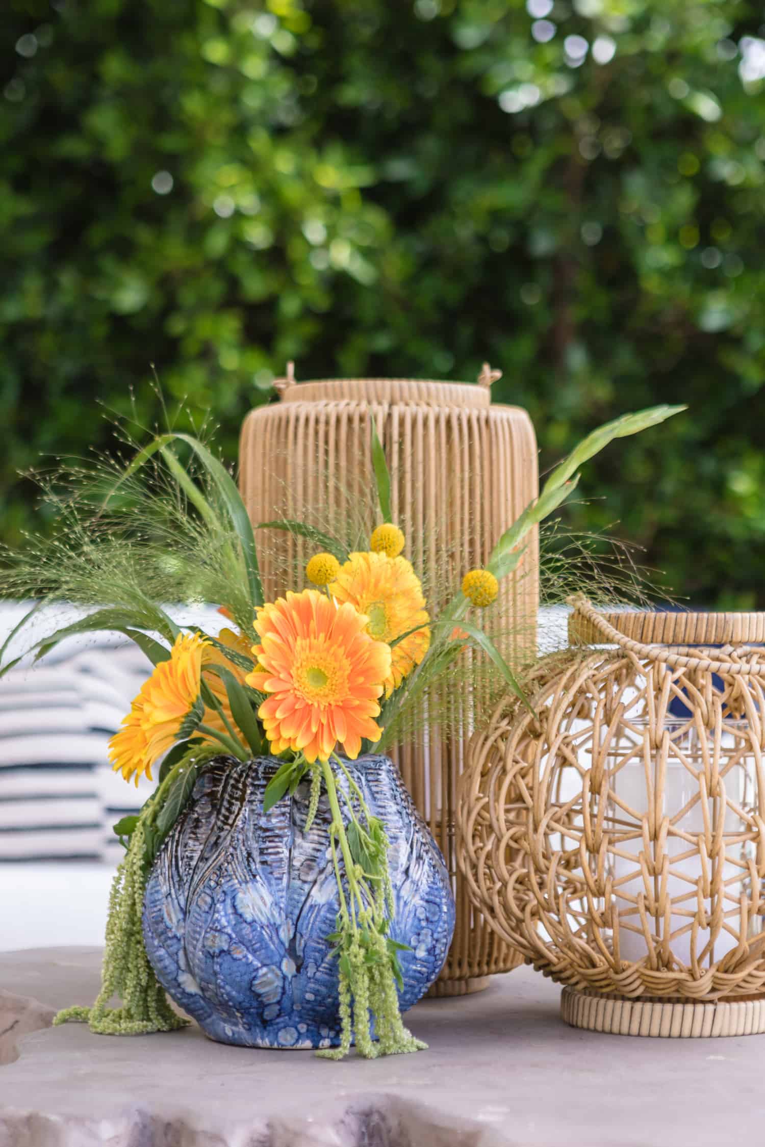 Close in shot of a simple centerpiece consisting of a blue vase with flowers, and two lanterns made of natural materials.