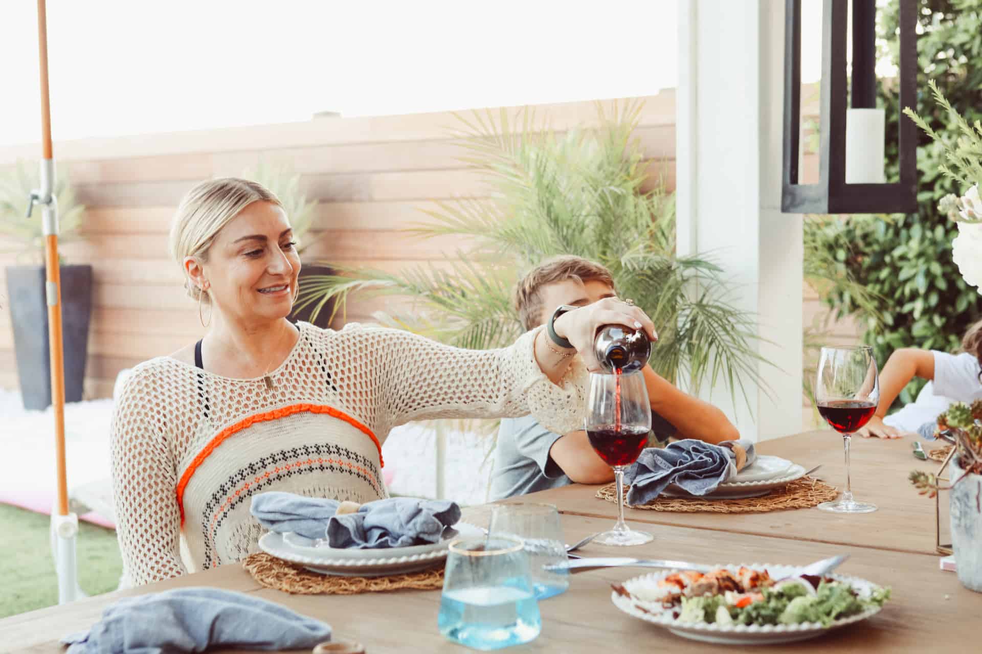 A family enjoying outdoor dining. An attractive woman is pouring a glass of wine.