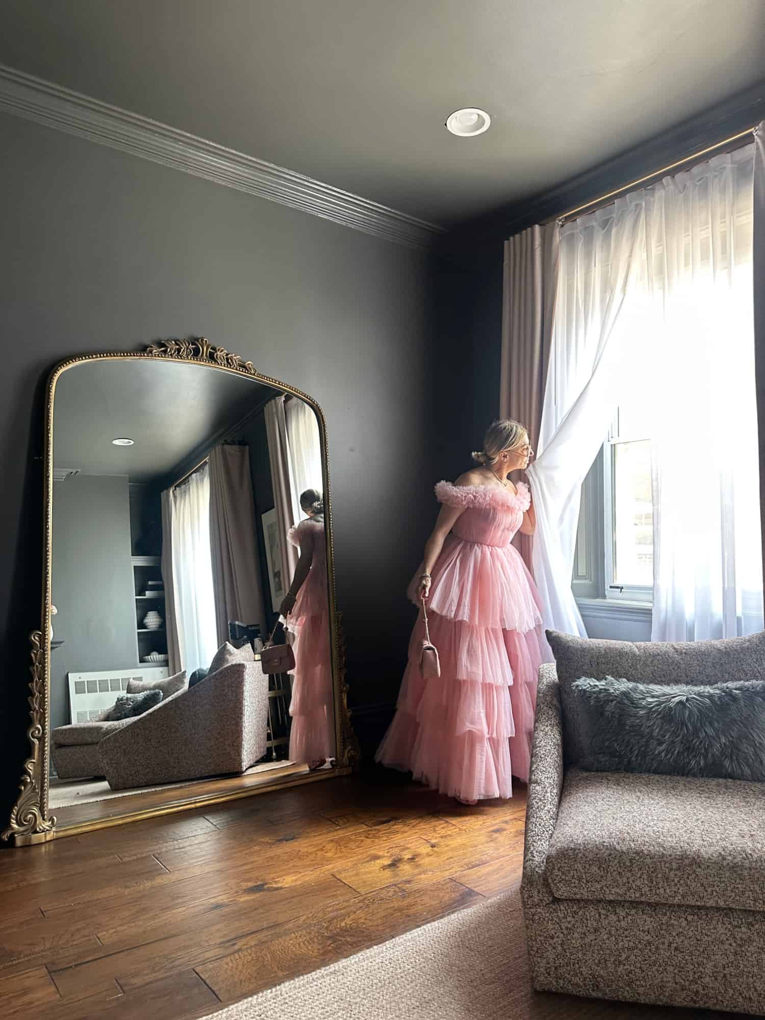 A woman wearing a fancy pink tulle dress in front of a large gilded mirror in The Gilded Queen Room suite in The Franklin on Rittenhouse.