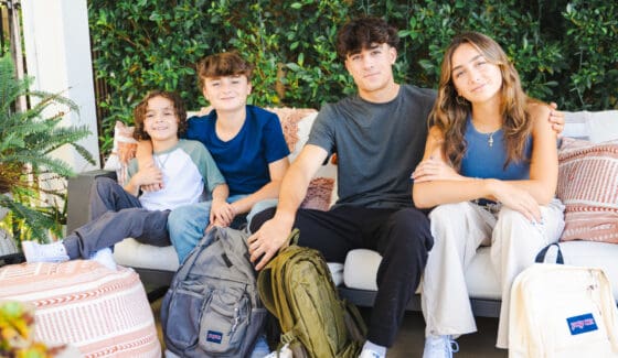 A family of 4 siblings. A young boy, tween boy, teen girl and teen boy sitting on an outdoor sofa wearing back to school clothes from Kohl's.