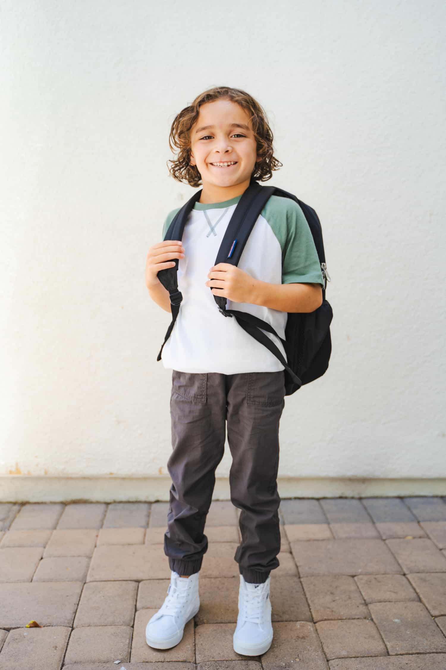 An adorable, smiling young boy wearing a backpack and looking ready for the new school year.
