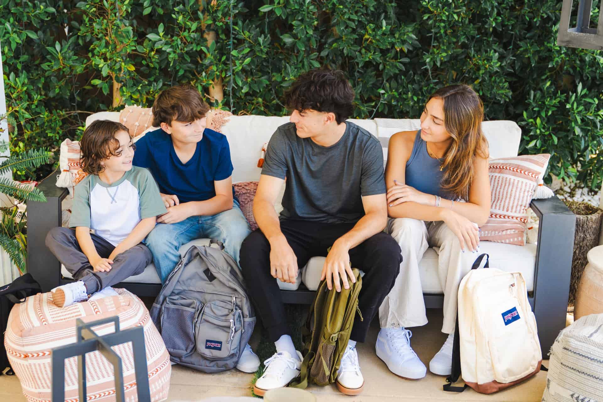 From left to right a young boy, tween boy, teen boy and teen girl sitting on an outdoor sofa. All are dressed in the latest back to school clothing trends from Kohl's. 