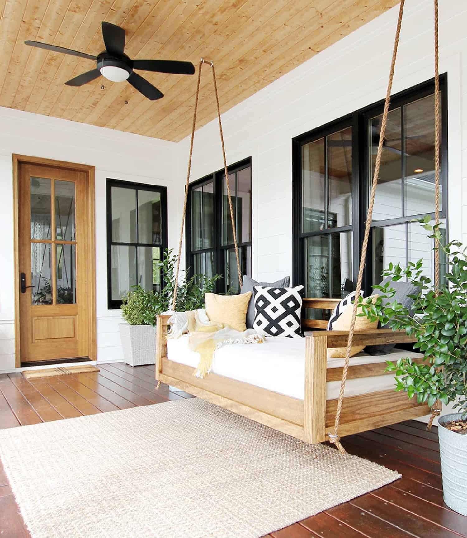 A large front porch decorated with neutral elements and a comfortable porch swing.